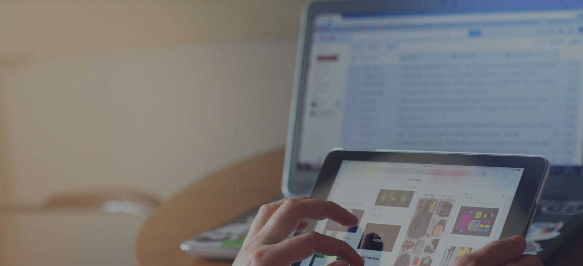 Birou cu laptop și o persoană care caută pe tabletă produse
